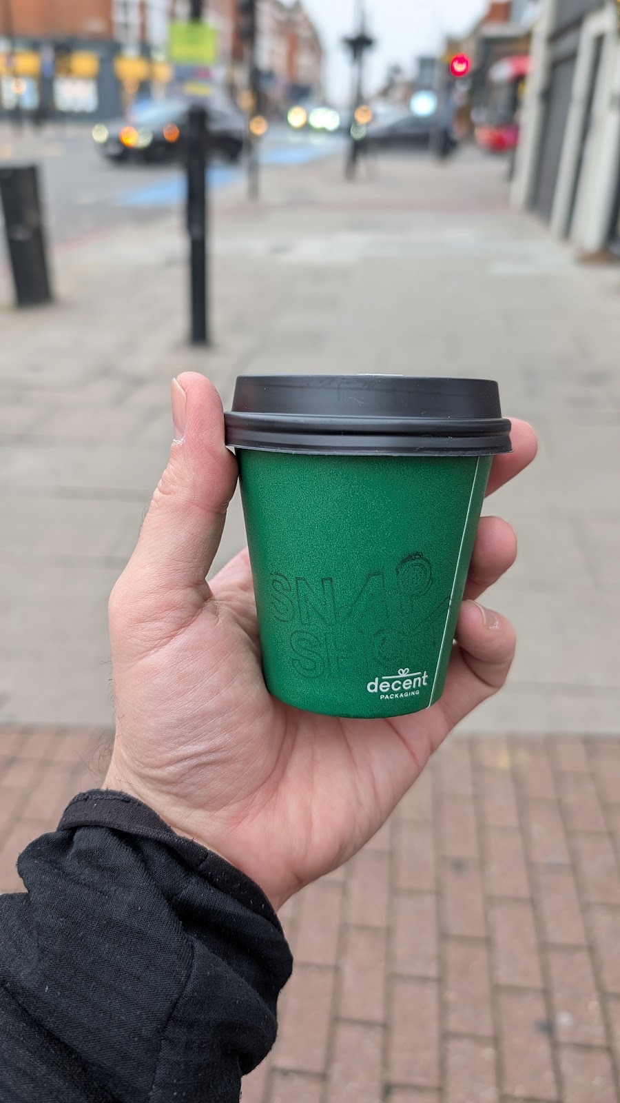 A hand holding a green takeaway cup on the high street
